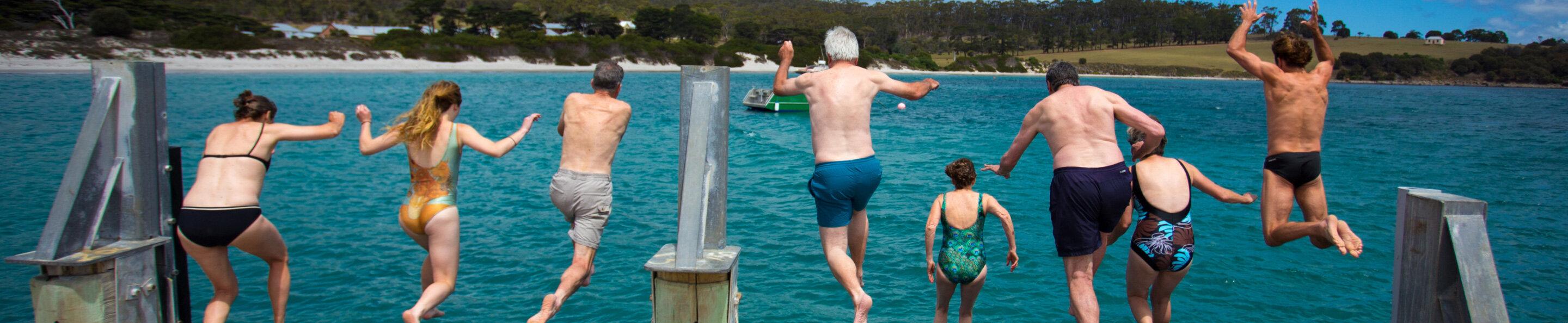 a group of swimmers jumping off a pier
