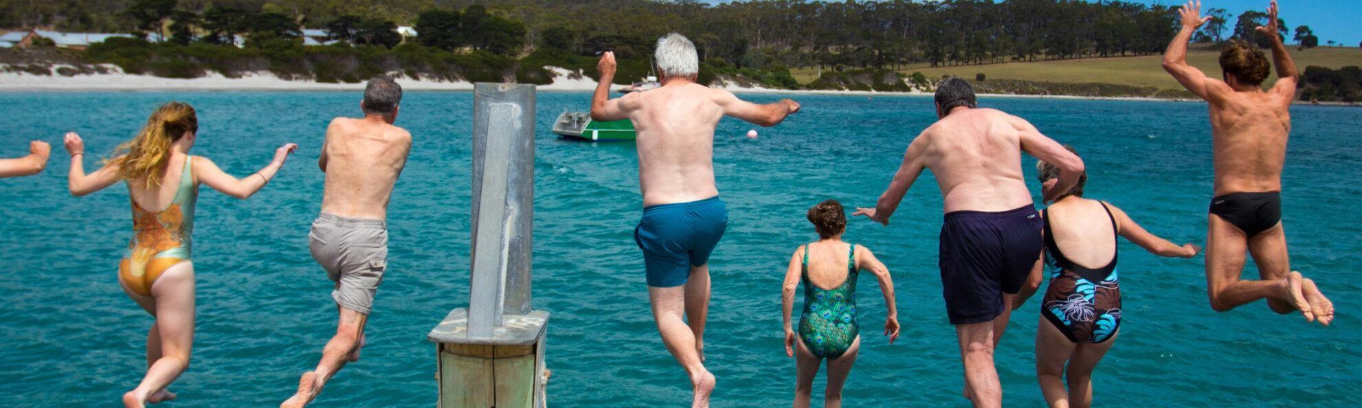 a group of swimmers jumping off a pier